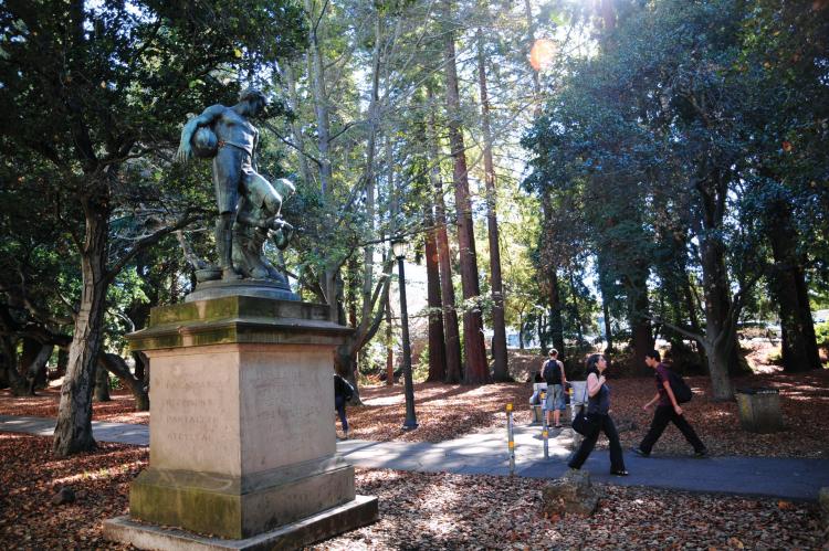 People walking on a path by the UC Berkeley Forest Statue on the University of California Berkeley campus.